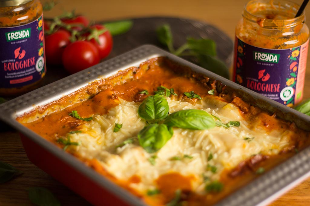 Vegane Lasagne Bolognese mit Froyda Sunflower Bolognese. Lasagne in Backform, daneben zwei leere Gläser Froyda Sunflower Bolognese, Tomaten und Basilikum.
