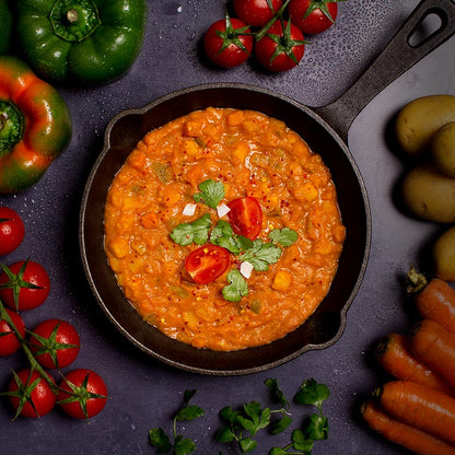 Froyda organic Madras curry in a pan, surrounded by fresh ingredients such as tomatoes, peppers, carrots and potatoes
