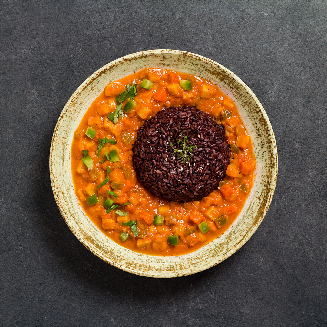 A plate of Madras Curry which consists of a tomato-based stew with potatoes and green bell peppers, served with red rice in the center.